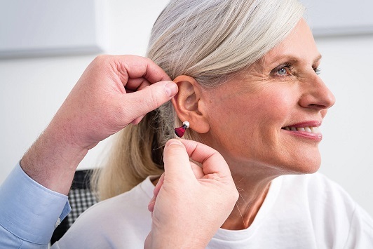 Ältere Frau bekommt ein modernes Hörgerät eingesetzt, Hörakustik Beratung im Alltag.